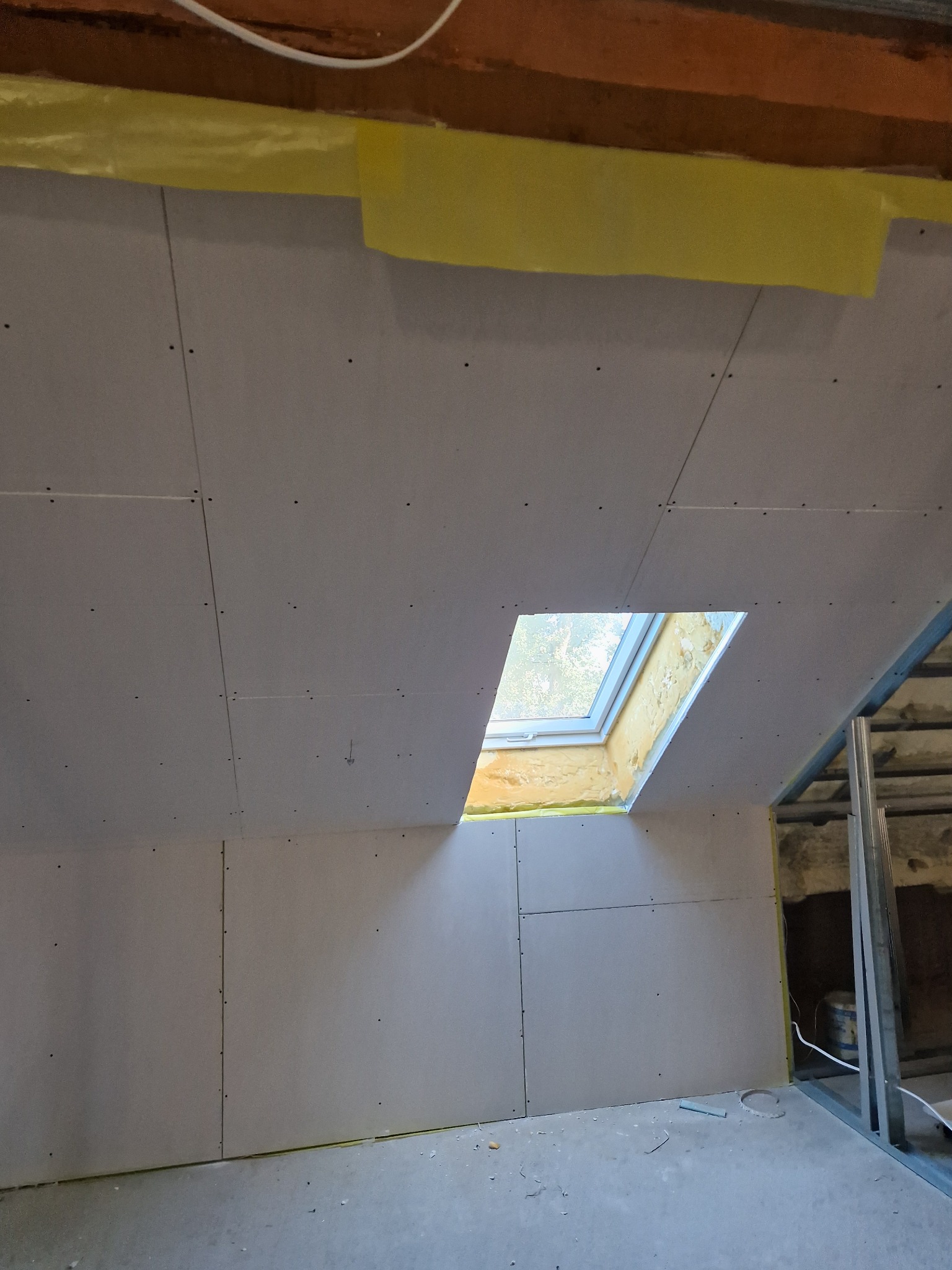 Montaż płyt na poddaszu z oknem dachowym, widoczne łączenia płyt i metalowa konstrukcja szkieletowa.