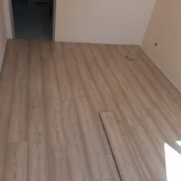 Układanie paneli podłogowych w jasnym odcieniu drewna, widoczny fragment nieukończonej podłogi i luźny panel.