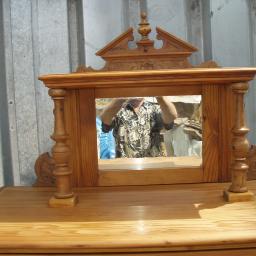 ADAM ARS MEBLE LITE DREWNO RENOWACJE. - Drewniana toaletka z lustrem w dekoracyjnej ramie, odbicie osoby w lustrze, surowe tło z blachy falistej.