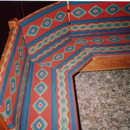 ADAM ARS MEBLE LITE DREWNO RENOWACJE. - Narożne siedzisko z drewnianą konstrukcją i tapicerką w czerwono-niebieskie wzory geometryczne, widoczne na tle mozaikowej podłogi.