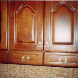 ADAM ARS MEBLE LITE DREWNO RENOWACJE. - Klasyczne, brązowe szafki kuchenne z drewnianymi frontami i ozdobnymi uchwytami, jedna z szafek przeszklona, widoczne płytki na ścianie.