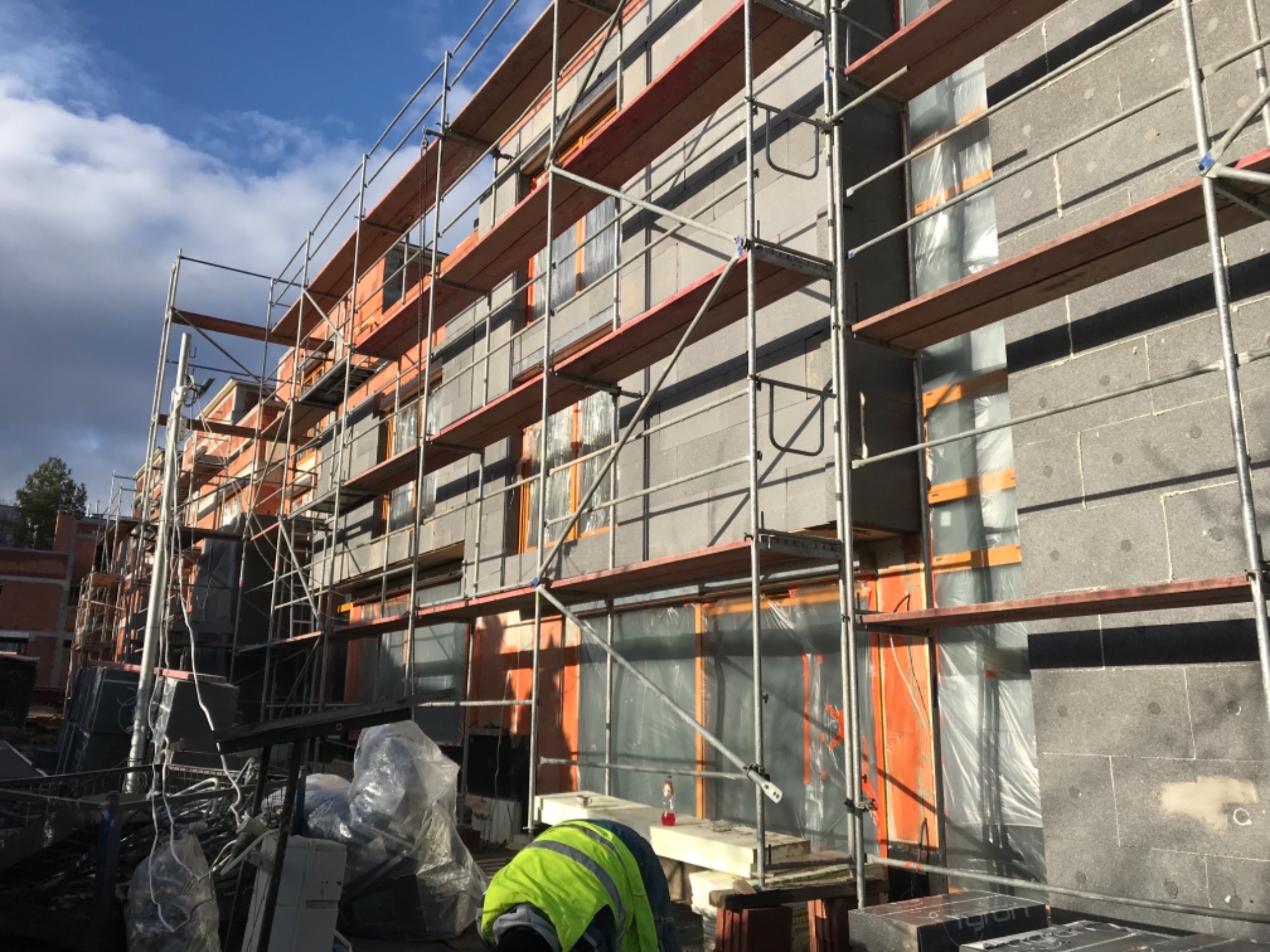 Budynek w Zawierciu w trakcie prac związanych z izolacją termiczną ścian zewnętrznych, widoczne rusztowania i przygotowane płyty izolacyjne.