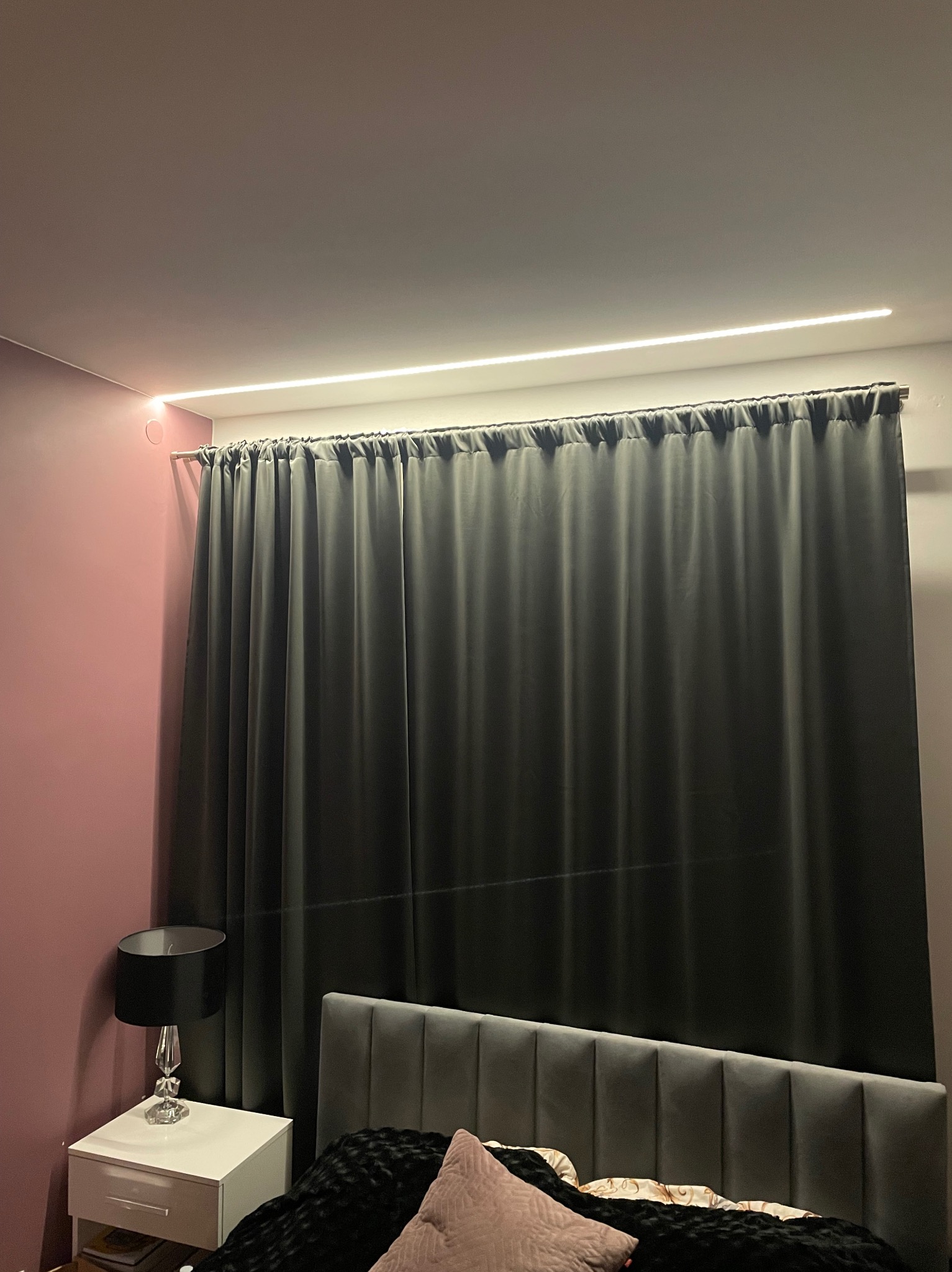 Pokój z szarą zasłoną, listwą LED podsufitową i lampką nocną na białej szafce