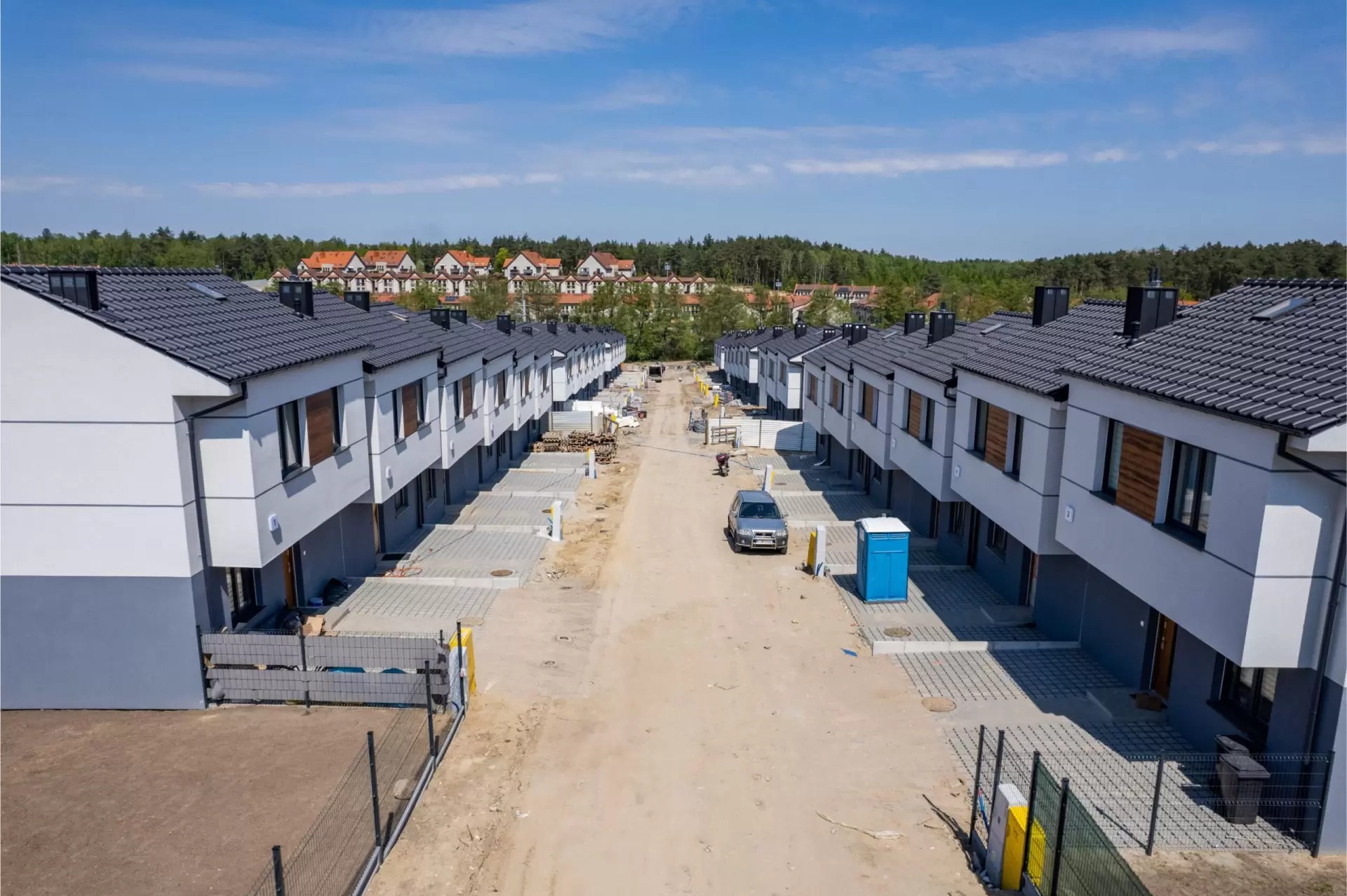 Nowe osiedle domów w trakcie budowy, widok z lotu ptaka, z widocznym pracownikiem i przenośną toaletą.