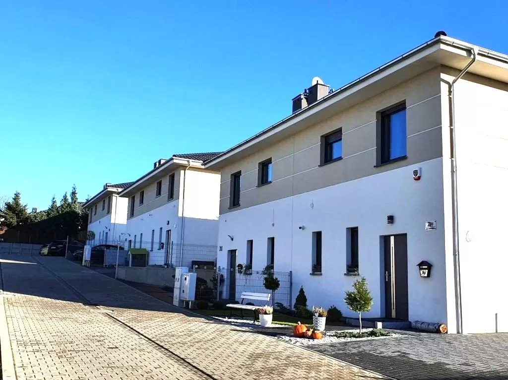 Szereg domów jednorodzinnych z płaskimi dachami, wykończonych w bieli i beżu, z dekoracjami jesiennymi przed wejściem.