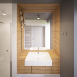 Katarzyna Steczko Widok Architekci - Nowoczesna łazienka z drewnianą zabudową umywalki, prostokątną białą umywalką nablatową i dużym lustrem w drewnianej ramie. W tle widoczny grzejnik drabinkowy i kabina prysznicowa.