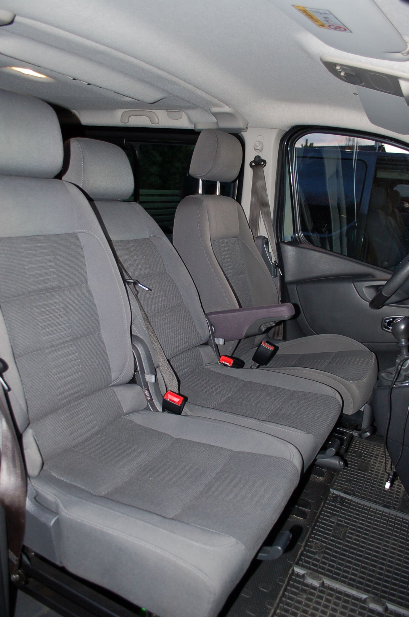 Wnętrze busa z trzema szarymi fotelami z pasami bezpieczeństwa i podłogą wyłożoną gumową kratką.