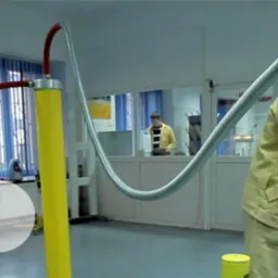 Pracownik w kombinezonie ochronnym w laboratorium wysokich napięć, regulujący aparaturę z izolatorami, przewodami i kulą elektrostatyczną.