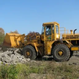 Żółta ładowarka kołowa marki Stalowa Wola nabiera gruz na terenie budowy w słoneczny dzień.