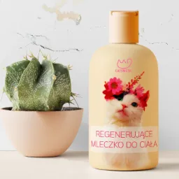 Krem regenerujący do ciała CATSMETIC z wizerunkiem kota w wianku z kwiatów, obok kaktus w beżowej doniczce na tle ściany z odpryskującą farbą.