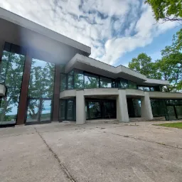 Nowoczesny budynek z dużymi przeszkleniami i aluminiowymi ramami okiennymi, otoczony zielenią. Widok z dołu, podkreślający architekturę budynku.