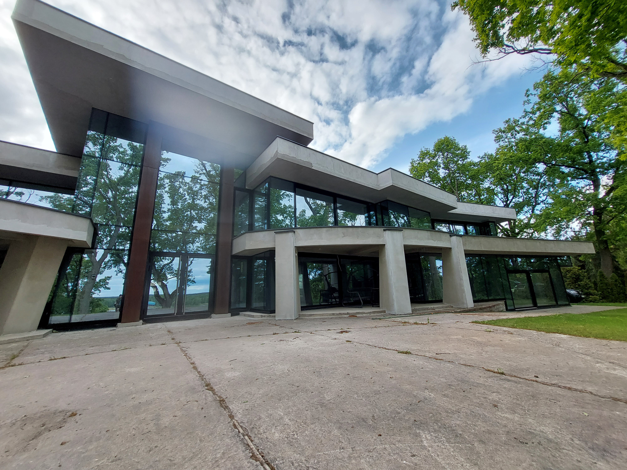 Nowoczesny budynek z dużymi przeszkleniami i aluminiowymi ramami okiennymi, otoczony zielenią. Widok z dołu, podkreślający architekturę budynku.