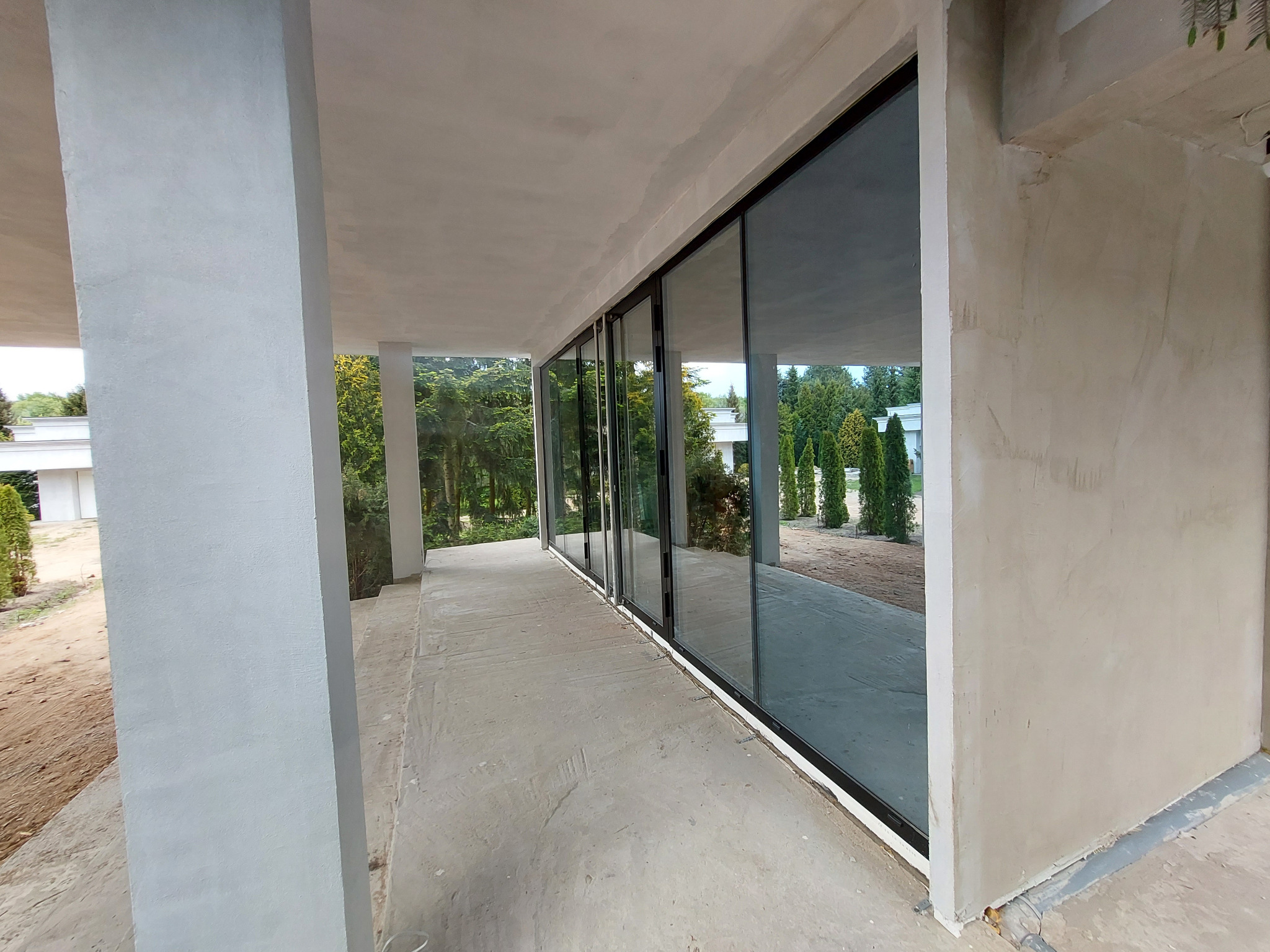 Nowoczesne, przesuwne okna z czarnymi ramami na tarasie, odbijające zieleń ogrodu. Widok na zewnątrz przez duże przeszklenia.