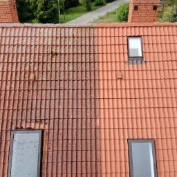 Częściowo wyczyszczony dach z czerwonej dachówki, widoczna wyraźna różnica między brudną i czystą powierzchnią, dwa okna dachowe i ceglany komin w tle.