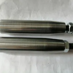 Dwa identyczne, metalowe, cylindryczne elementy z gwintem i nakrętkami na końcach, leżące równolegle na białym tle. Widoczne ślady obróbki mechanicznej na powierzchni.