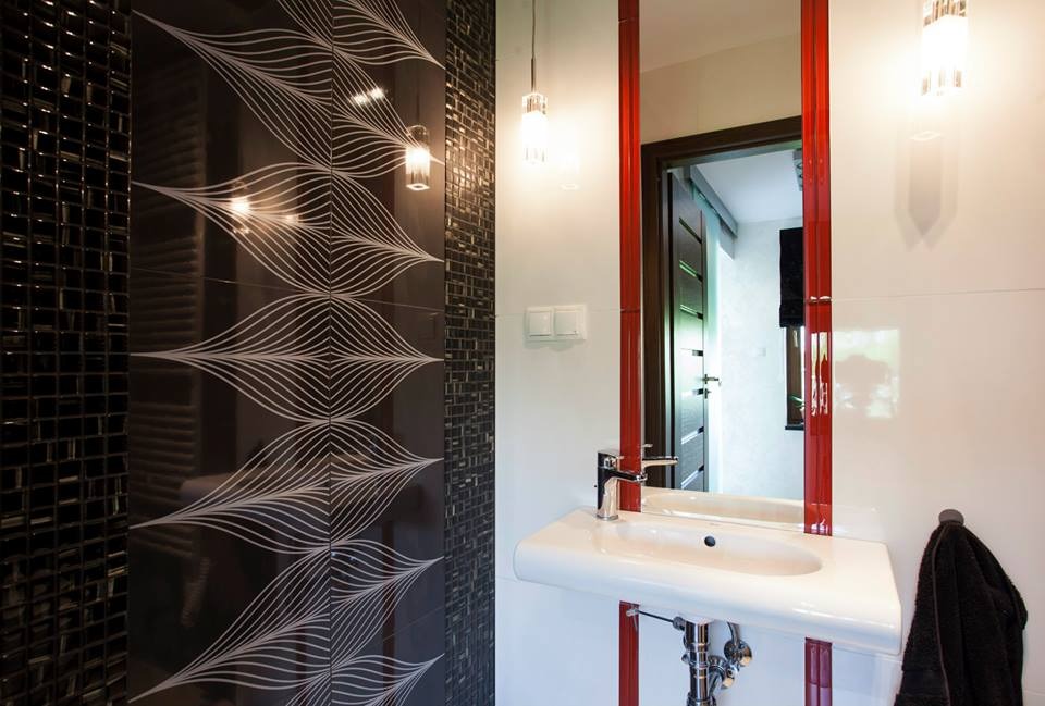 Nowoczesna łazienka z czarno-białymi płytkami z motywem fal, umywalką na postumencie i lustrem w czerwonej ramie.