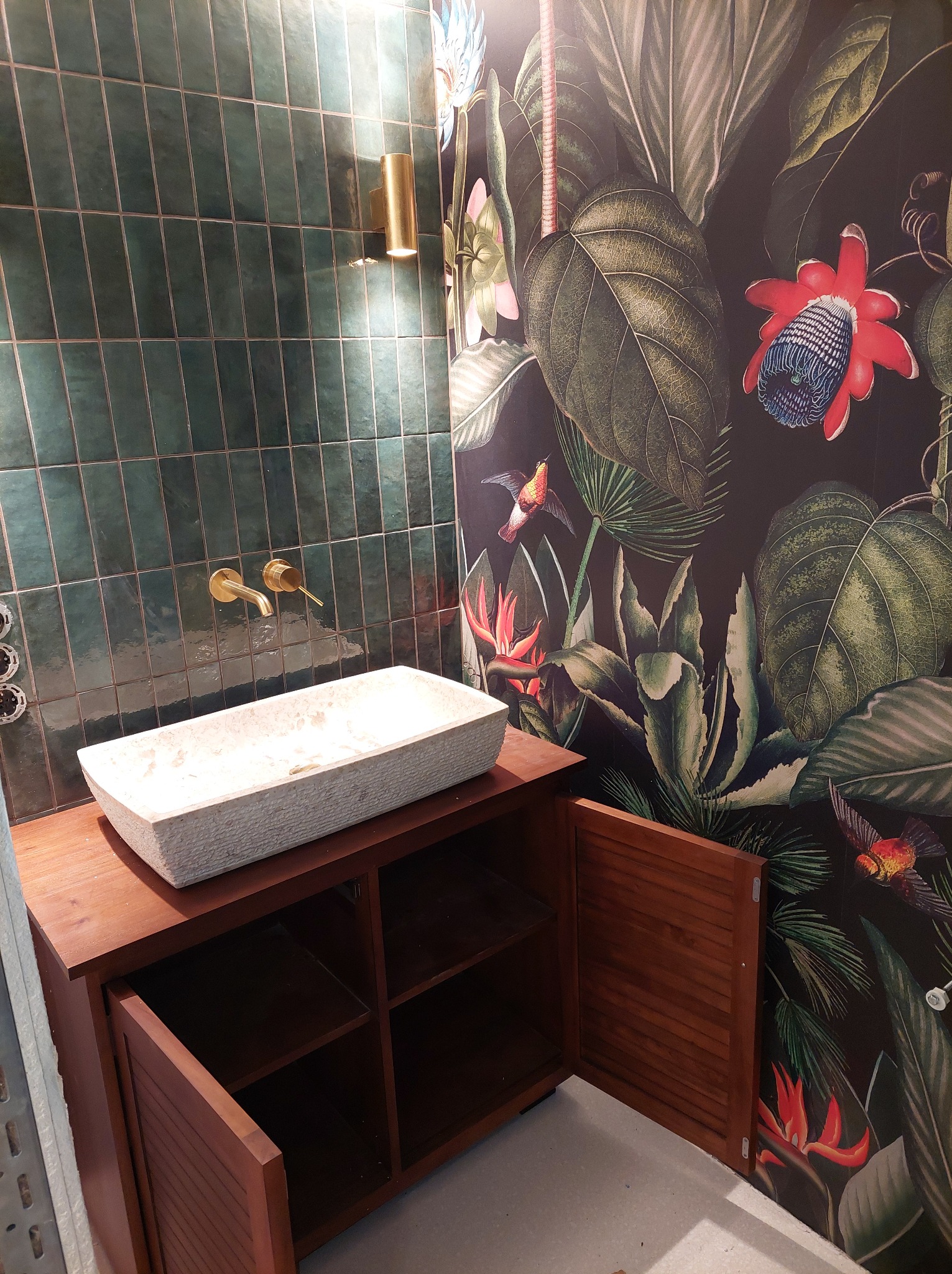 Egzotyczna łazienka: zielone, pionowe płytki, złota armatura, kamienna umywalka na drewnianej szafce, ściana w tropikalne wzory. Nowoczesny design.