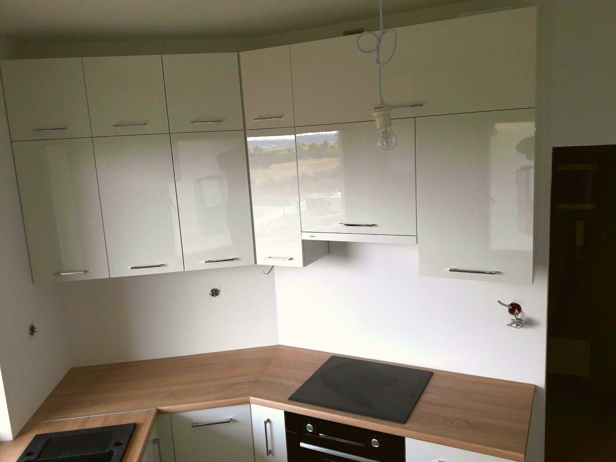 Nowoczesna kuchnia z białymi, lakierowanymi szafkami, drewnianym blatem i czarną płytą indukcyjną, widoczne niedokończone prace elektryczne.