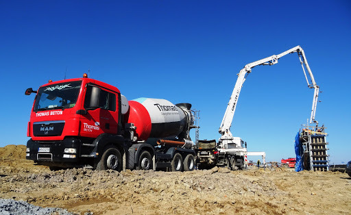 Czerwona betonomieszarka z wysięgnikiem pompuje mieszankę do szalunku na budowie w słoneczny dzień.