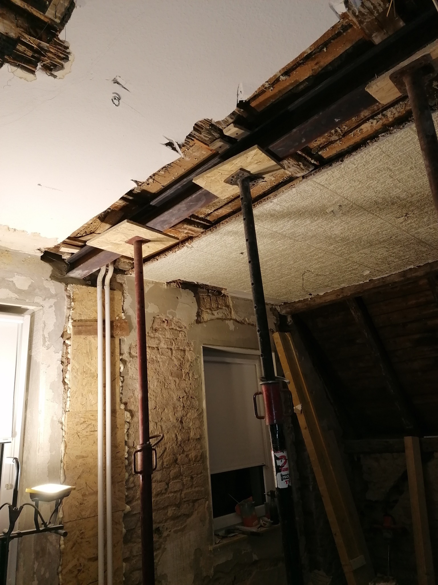 Wnętrze w trakcie prac remontowych, widoczne podpory stropowe, odsłonięta konstrukcja sufitu i fragmenty starej instalacji elektrycznej