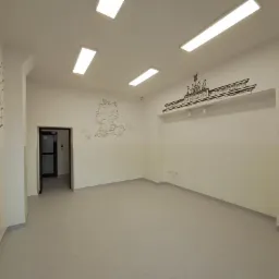 Pomalowane na jasno wnętrze biurowe z rysunkami na ścianach: mapa Niemiec i Brama Brandenburska. Widoczne prostokątne lampy sufitowe i wejście do innego pomieszczenia.