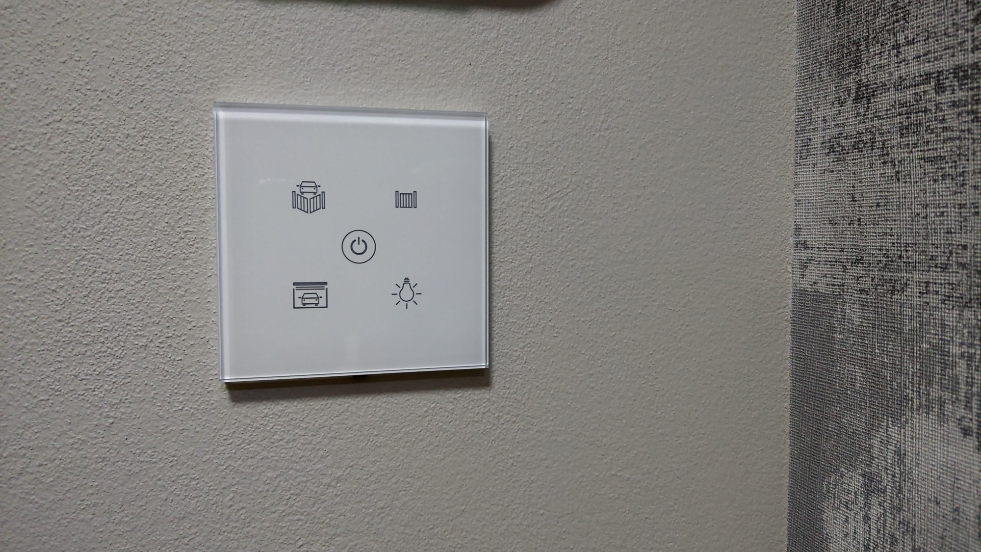 Szklany panel dotykowy na ścianie, z ikonami sterowania bramą wjazdową, garażową, furtką, włącznikiem i regulacją oświetlenia.