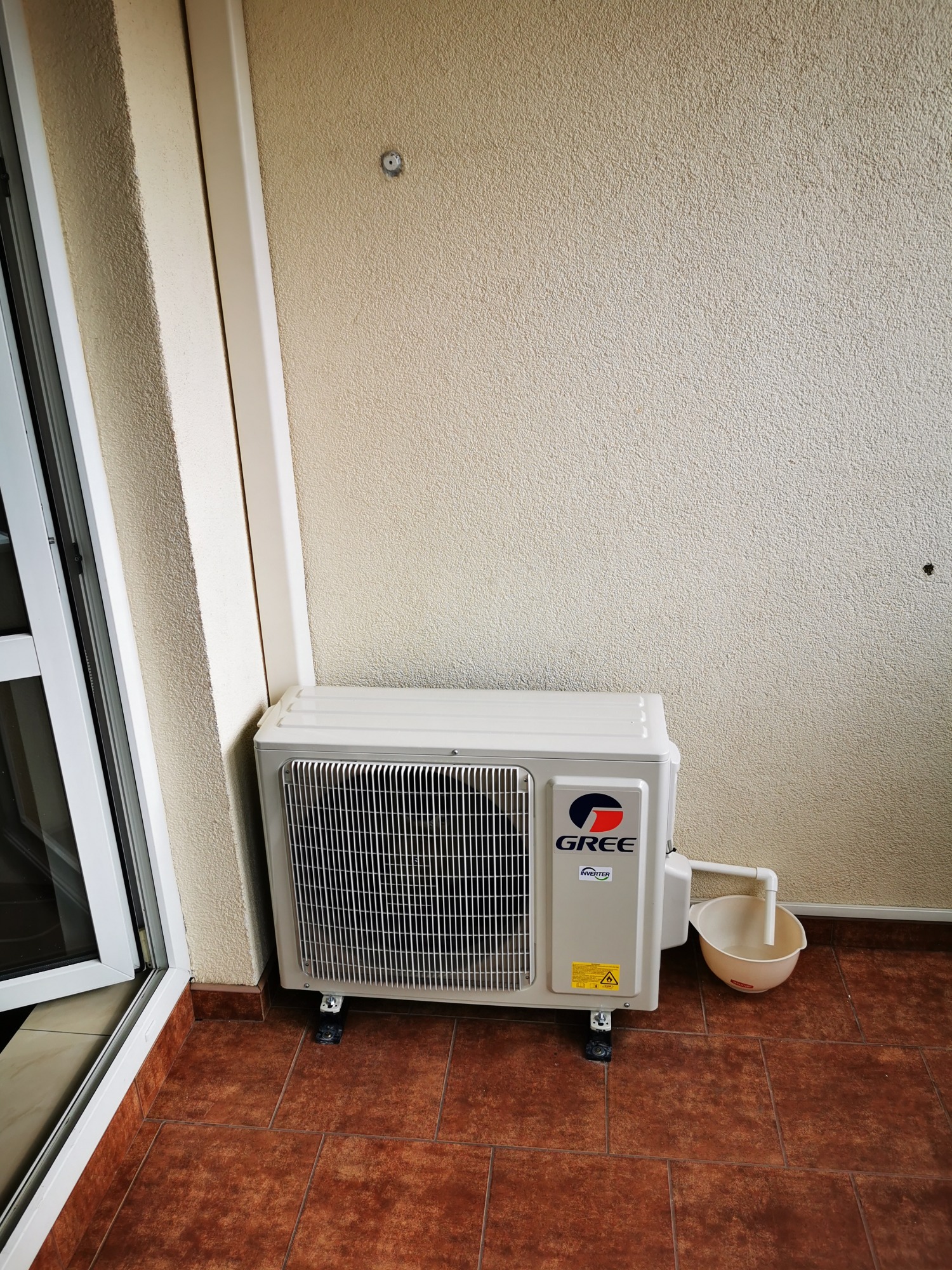 Zewnętrzna jednostka klimatyzacji marki Gree na balkonie, z odprowadzeniem skroplin do plastikowego pojemnika.