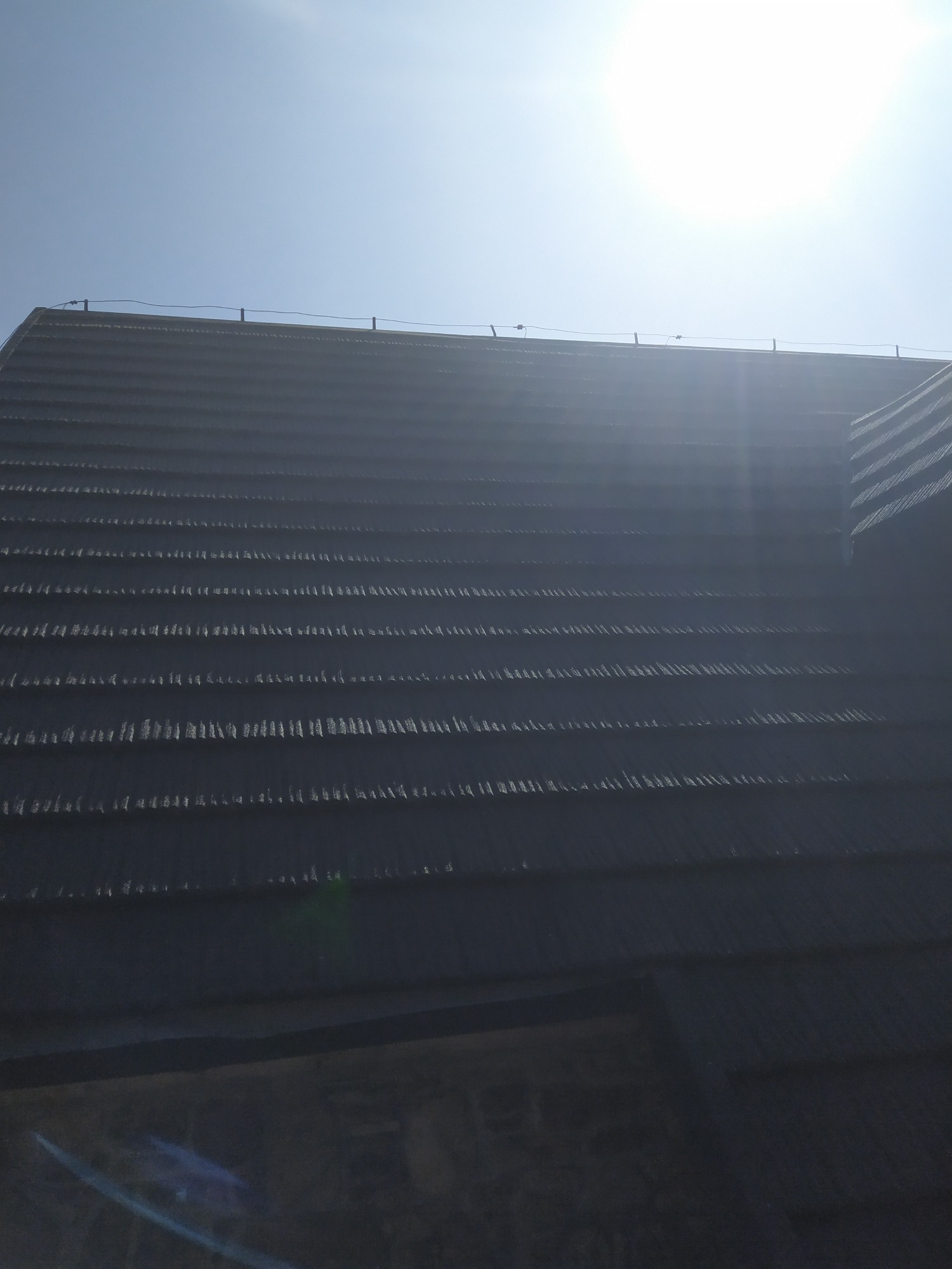 Nowy dach z ciemnej dachówki ceramicznej, widok od dołu w słoneczny dzień, z widocznymi elementami zabezpieczenia przeciwoblodzeniowego.