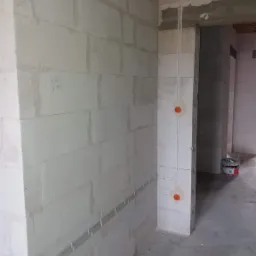 Instalacja elektryczna w surowym wnętrzu: kable prowadzone w listwach przypodłogowych, pionowe przewody wychodzące z puszek instalacyjnych w ścianie z betonu komórkowego, widoczny fragment...