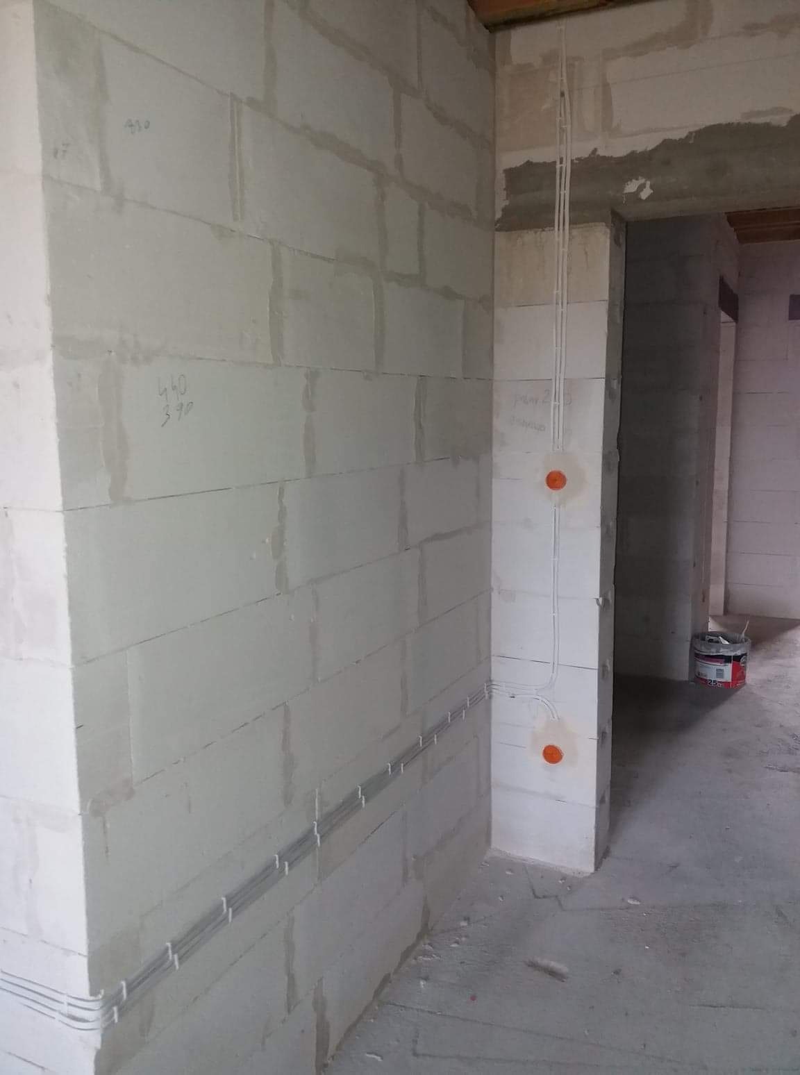 Instalacja elektryczna w surowym wnętrzu: kable prowadzone w listwach przypodłogowych, pionowe przewody wychodzące z puszek instalacyjnych w ścianie z betonu komórkowego, widoczny fragment...