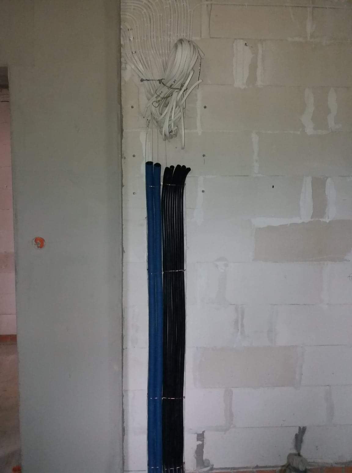 Wiązki przewodów elektrycznych w peszlach (niebieski i czarny) oraz luźne przewody ułożone przy ścianie z betonu komórkowego w surowym stanie.