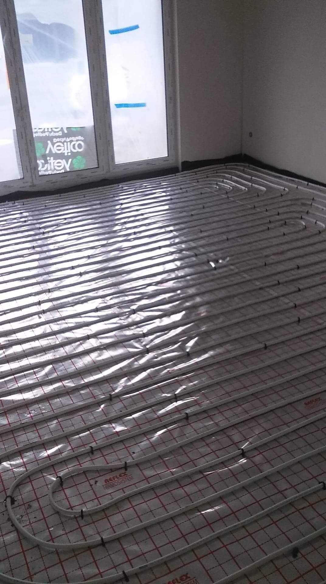 Instalacja ogrzewania podłogowego w Rząśniku, widoczne białe rurki ułożone na folii z czerwoną siatką, przygotowane do zalania wylewką.