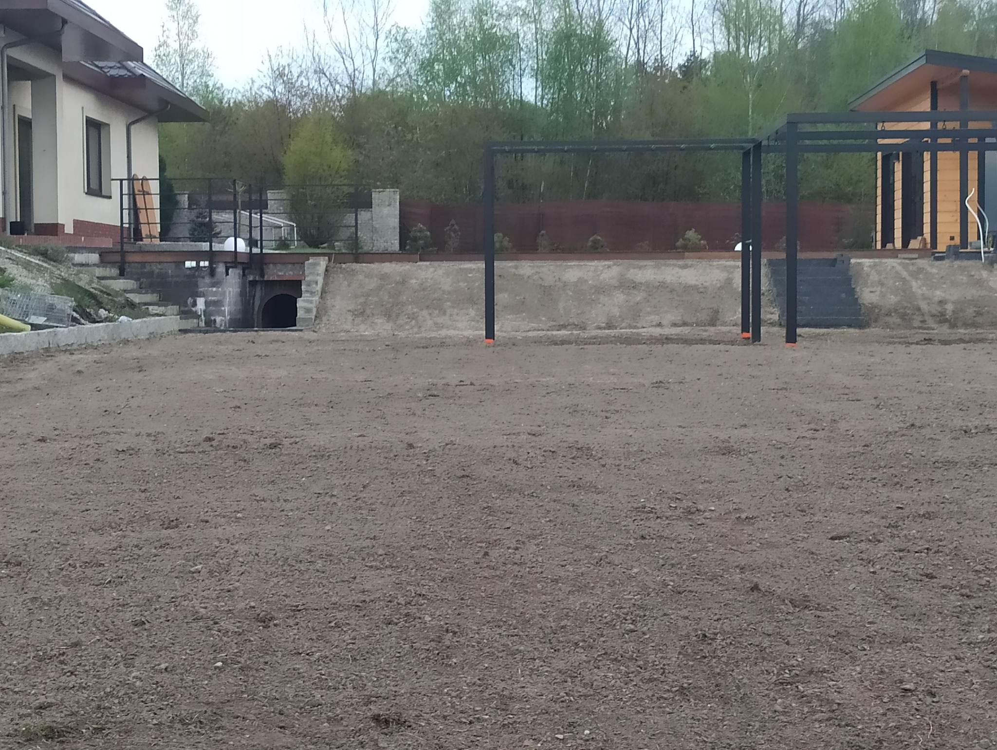 Przygotowany teren pod budowę z widoczną konstrukcją pergoli, domem w tle i tunelem odprowadzającym wodę.
