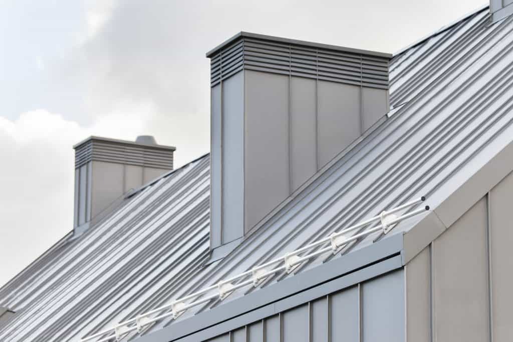 Szary dach z blachy trapezowej z dwoma kominami wentylacyjnymi i zabezpieczeniem przeciwśniegowym, widok z dołu.