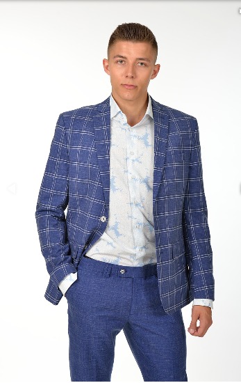 Młody mężczyzna w niebieskim garniturze w kratę i koszuli z delikatnym wzorem, pozujący na białym tle.