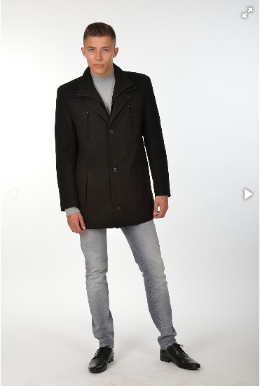 Mężczyzna prezentuje czarny, wełniany płaszcz z trzema guzikami, szarą bluzkę i jeansy na jasnym tle.