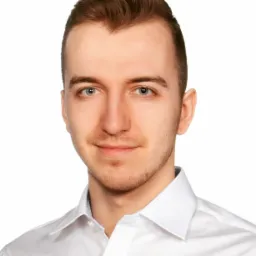 Portret młodego mężczyzny z krótkimi brązowymi włosami i lekkim zarostem, ubranego w białą koszulę na jasnym tle.