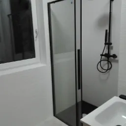 Nowoczesna łazienka z kabiną prysznicową typu walk-in z czarnymi profilami, deszczownicą i armaturą w kolorze czarnym, umywalką nablatową na szafce, wykończona płytkami imitującymi kamień w jasnych...