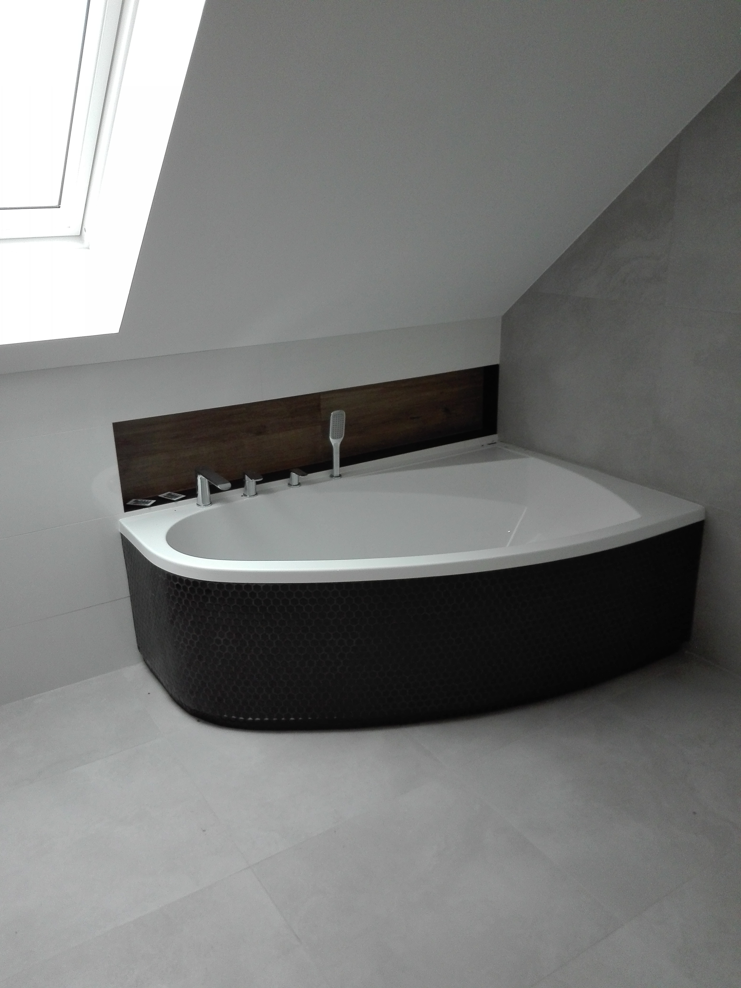 Narożna wanna z czarną mozaiką w łazience na poddaszu w Makowie Mazowieckim, widok z góry, jasne płytki podłogowe i okładzina ściany.