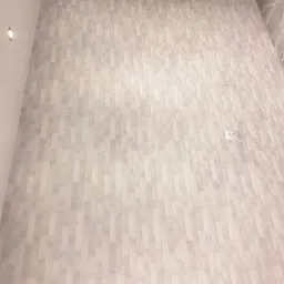 Jasnoszara ściana wyłożona pionowymi, prostokątnymi płytkami imitującymi kamień, z widocznym gniazdkiem elektrycznym i oświetleniem punktowym.