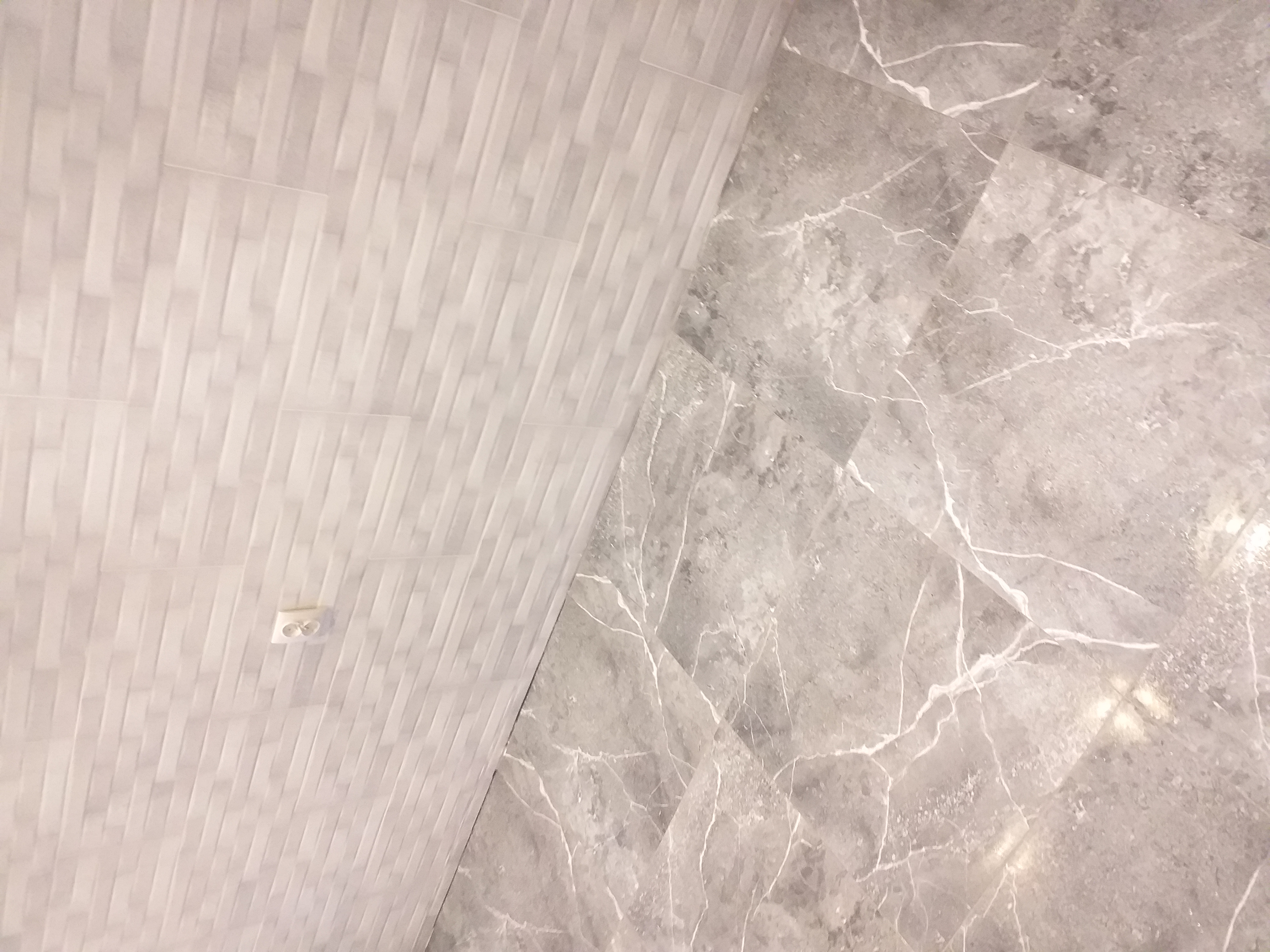 Połączenie białej, panelowej ściany z szarą ścianą imitującą marmur z widocznym gniazdkiem elektrycznym na białej ścianie.