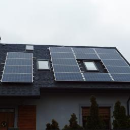 Fi-Ma Group Przemysław Hendrysiak - Panele słoneczne zamontowane na dachu domu jednorodzinnego z oknami dachowymi, widok z dołu na szarym tle nieba.