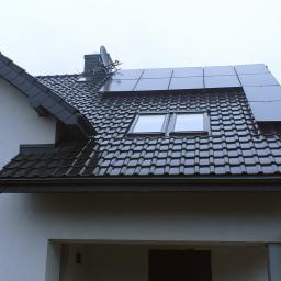 Fi-Ma Group Przemysław Hendrysiak - Dom jednorodzinny z ciemną dachówką, oknami dachowymi i zamontowanymi panelami fotowoltaicznymi na części dachu.