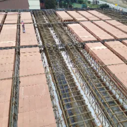 Zbrojenie stropu Teriva z pustakami ceramicznymi, widoczni pracownicy w odblaskowych kurtkach, puszka pianki montażowej na pustaku.