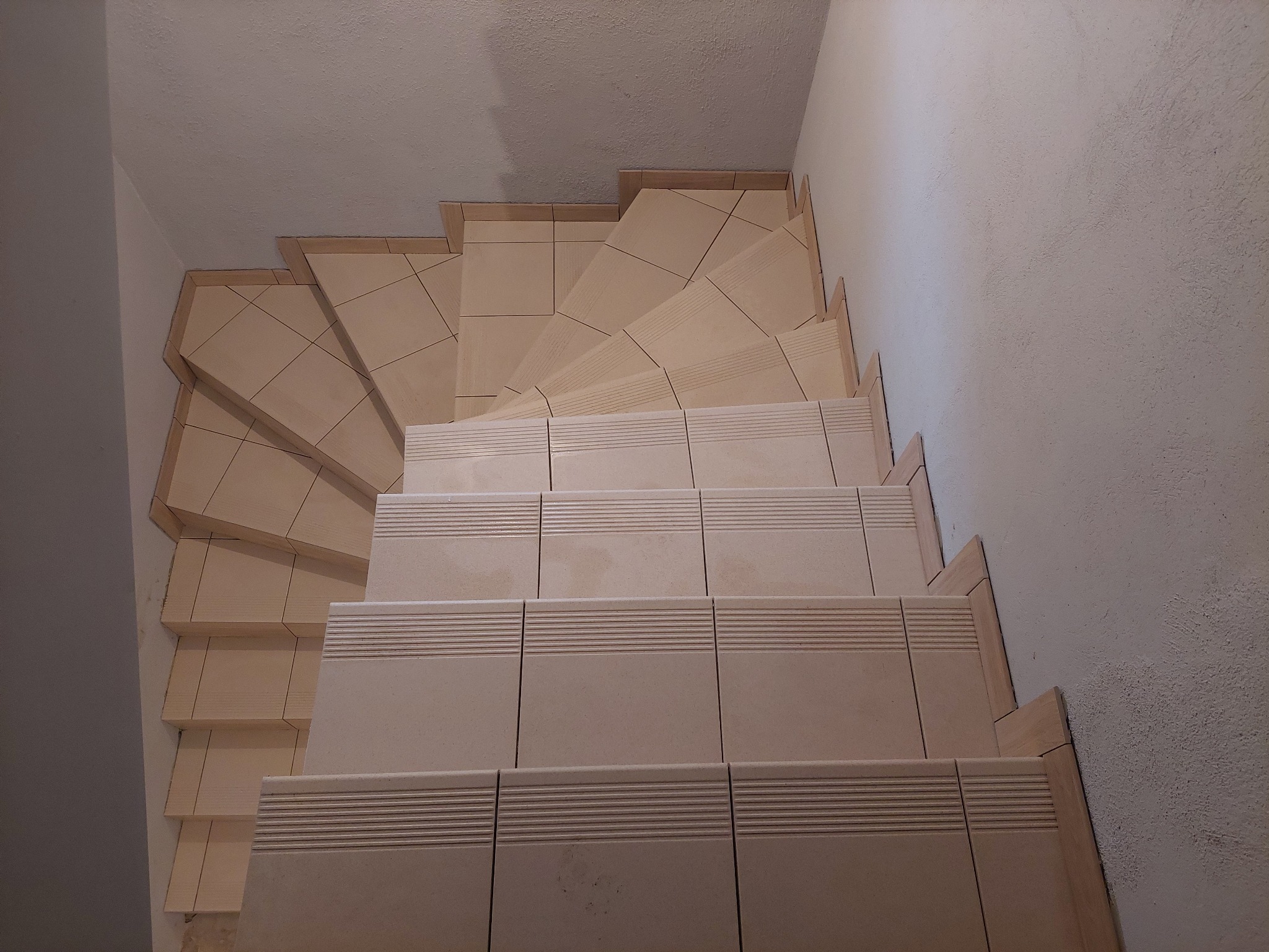 Wykończone schody z beżowych płytek ceramicznych z ryflowanymi krawędziami, widoczne z góry, ściana pomalowana na biało z widoczną strukturą.