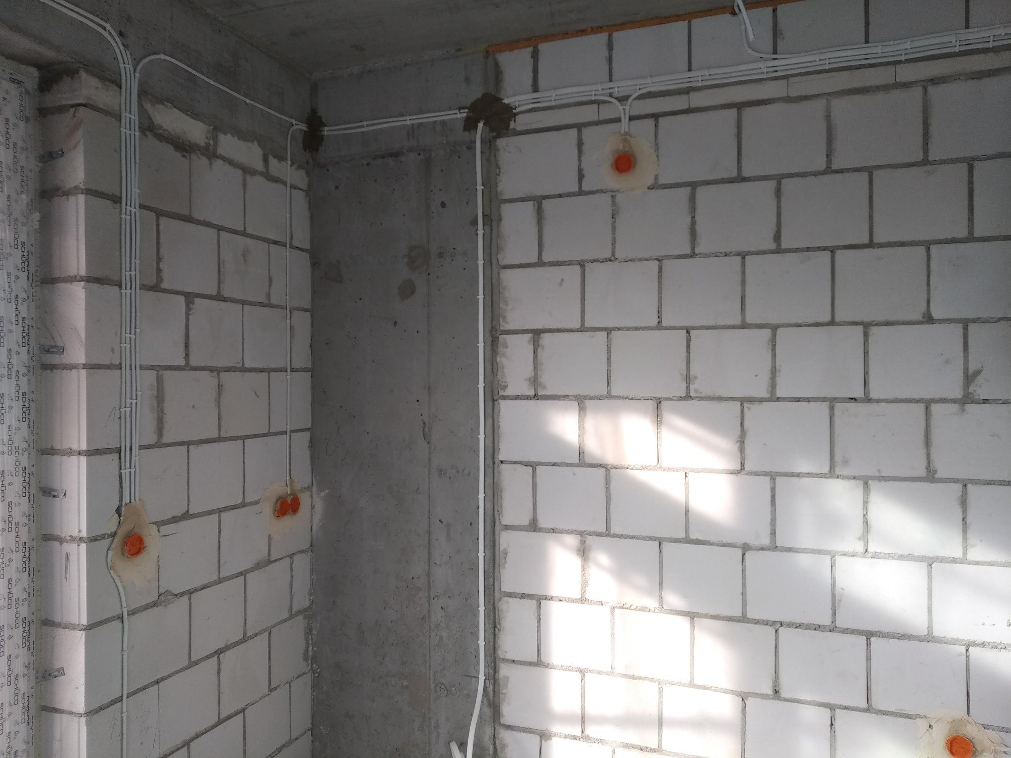 Surowy stan: Białe przewody elektryczne prowadzone po ścianach z betonu komórkowego i surowego betonu, widoczne puszki instalacyjne z pomarańczowymi dekielkami.