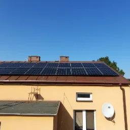 Brązowy dach domu z panelami słonecznymi w słoneczny dzień. Drewniana drabina oparta o ścianę, a na dachu krzesło.