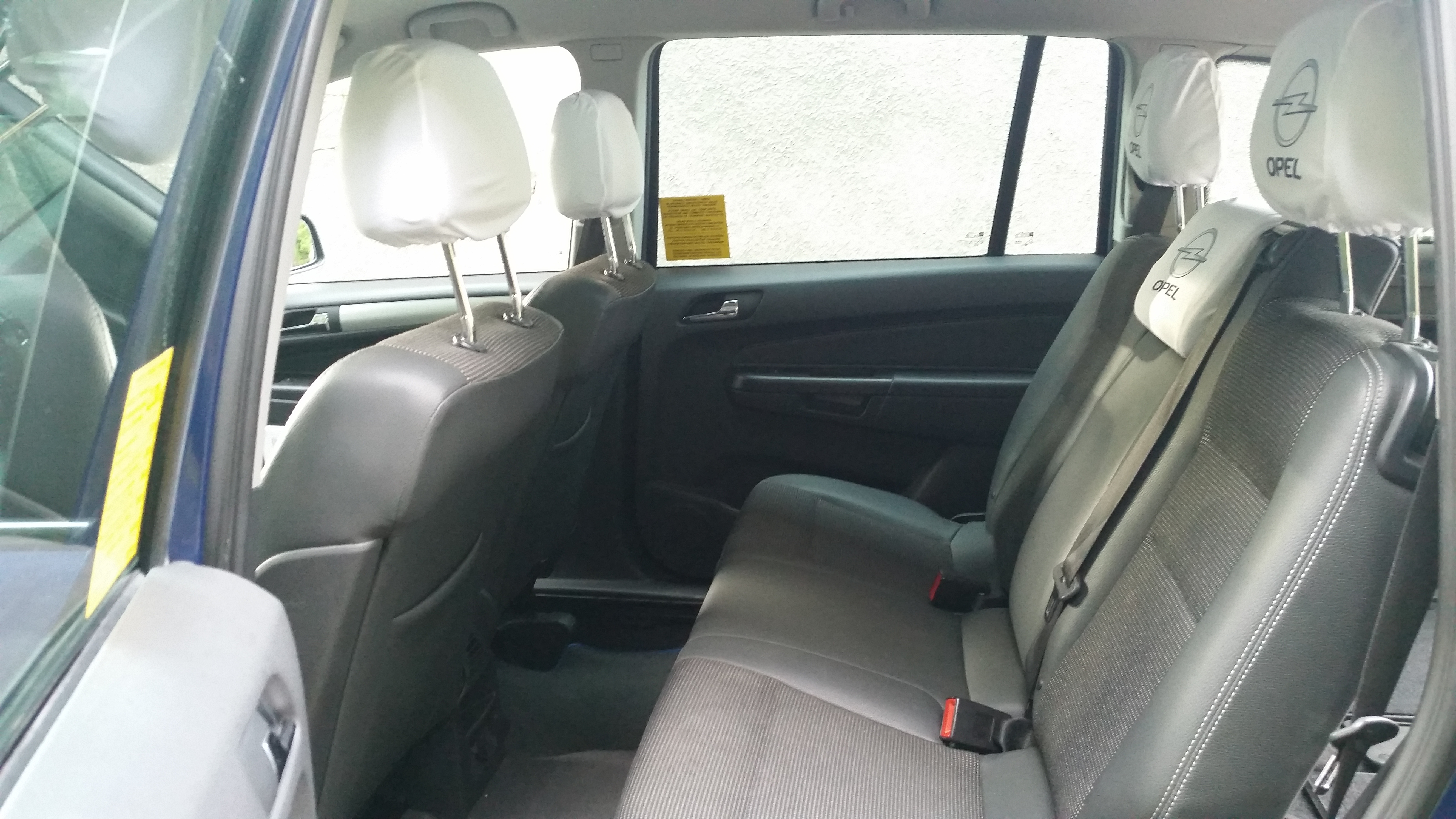Wnętrze samochodu Opel Zafira z szarymi siedzeniami i pokrowcami na zagłówkach z logo firmy, widok z tylnych drzwi.