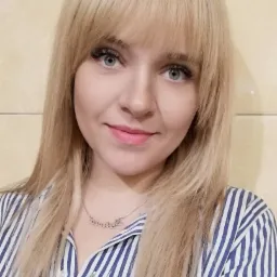 Portret uśmiechniętej blondynki w niebiesko-białej koszuli w paski, z delikatnym makijażem i srebrnym naszyjnikiem z napisem.