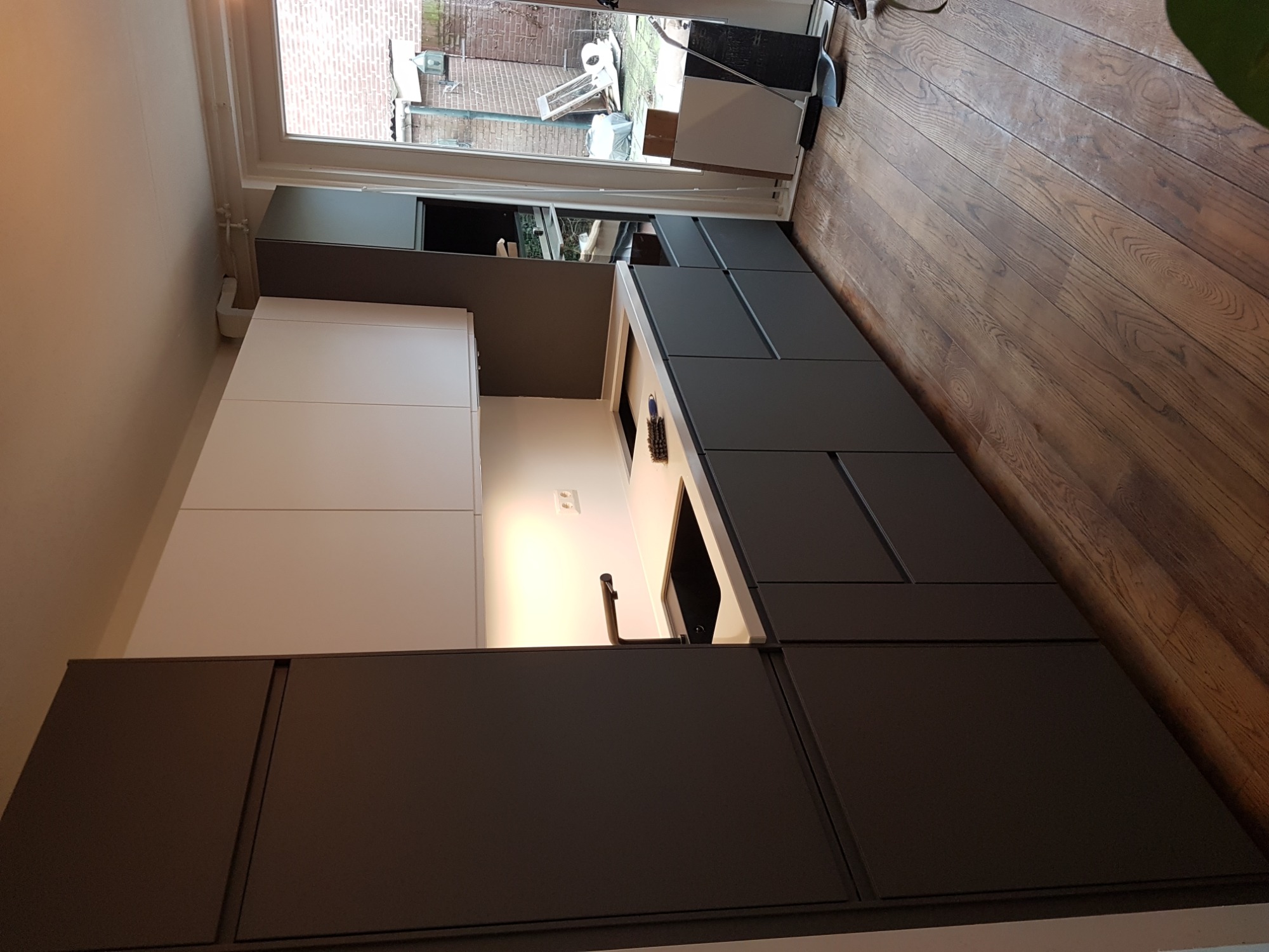 Nowoczesna kuchnia z szarymi szafkami dolnymi i białymi górnymi, drewniana podłoga, widok na ogród przez otwarte drzwi balkonowe.